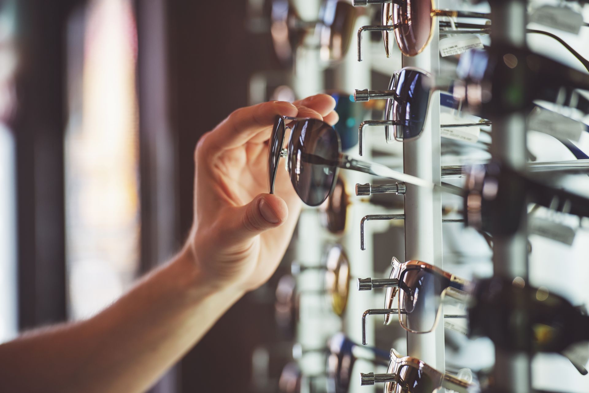 Hand selecting sunglasses from a display rack in an eyewear store.