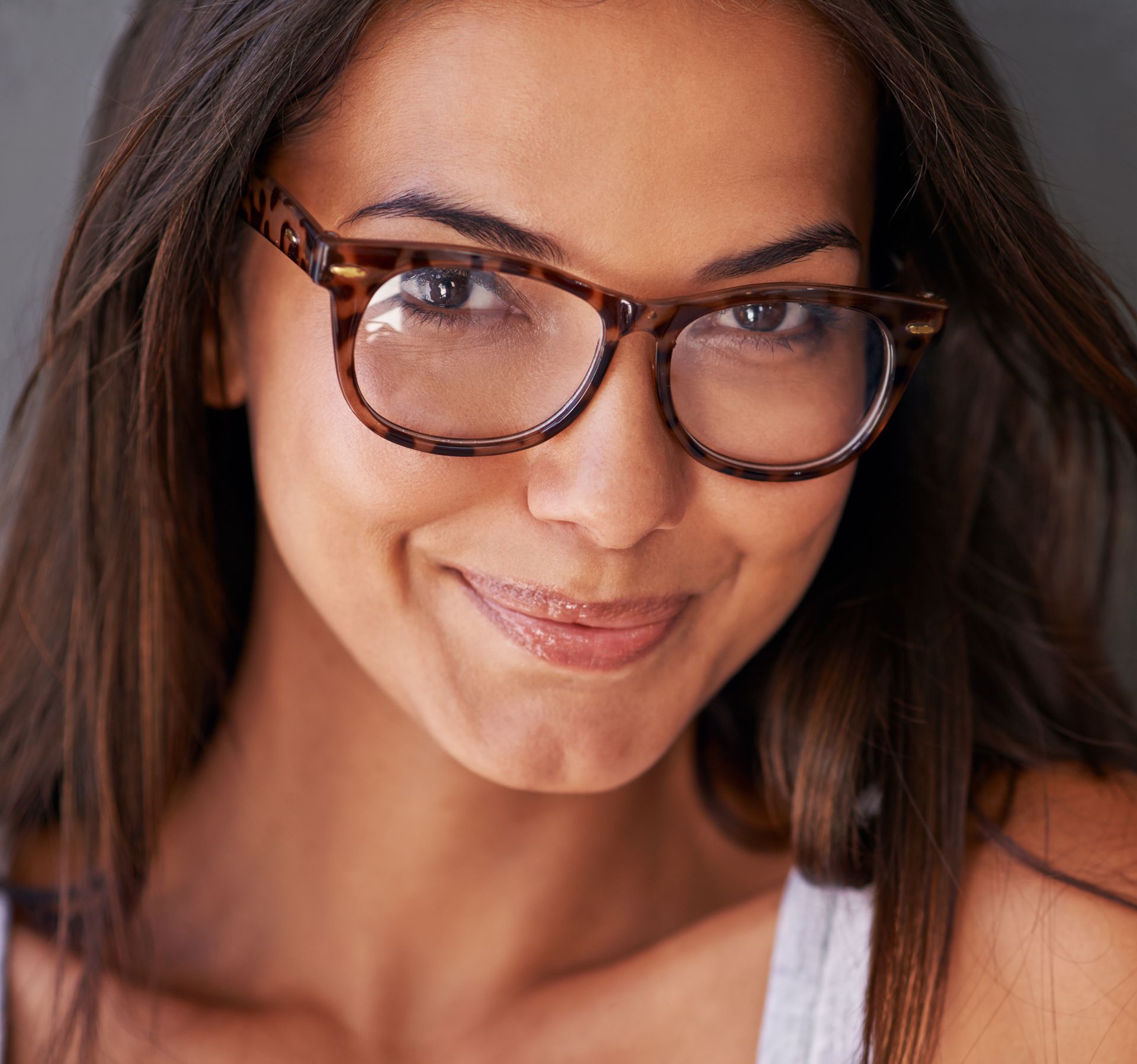 A smiling woman with long brown hair wearing tortoiseshell designer eyeglass frames