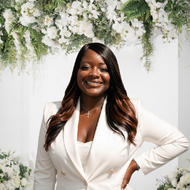 Smiling woman in a black-and-white striped blazer standing outdoors in sunlight