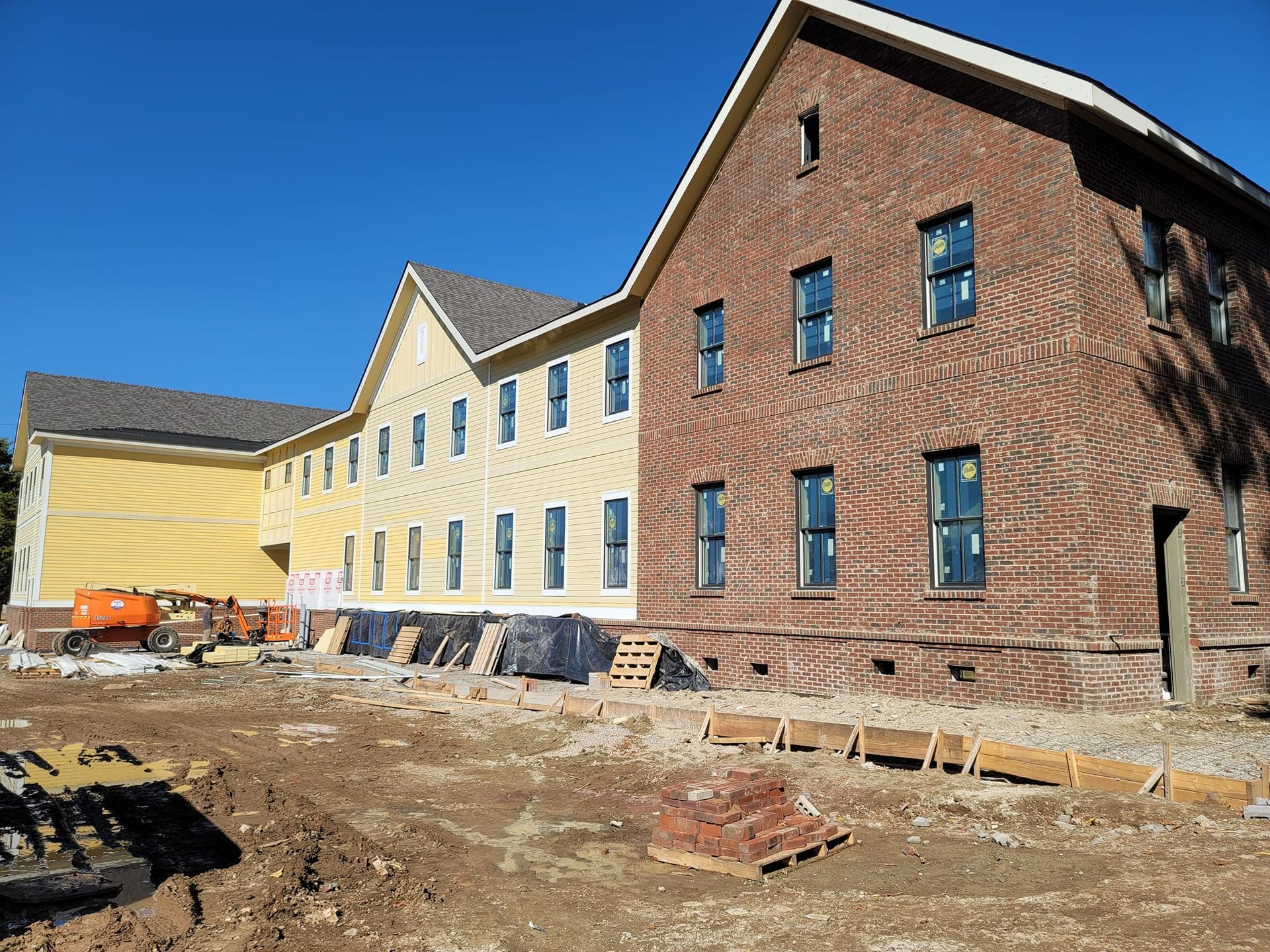 Construction site with yellow clapboard and brick buildings against a blue sky.