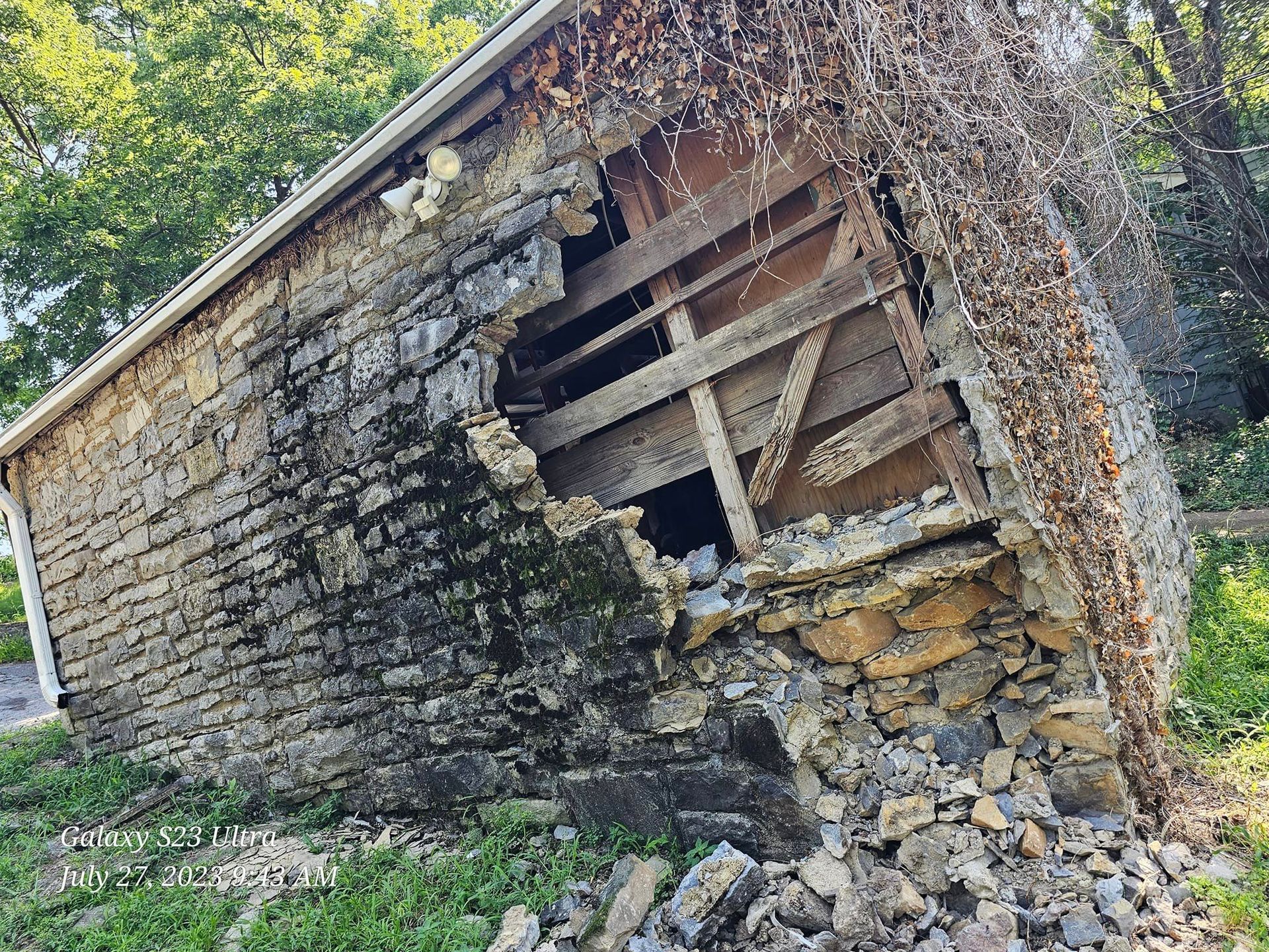 Dilapidated stone building with missing wall sections; vines grow over it.