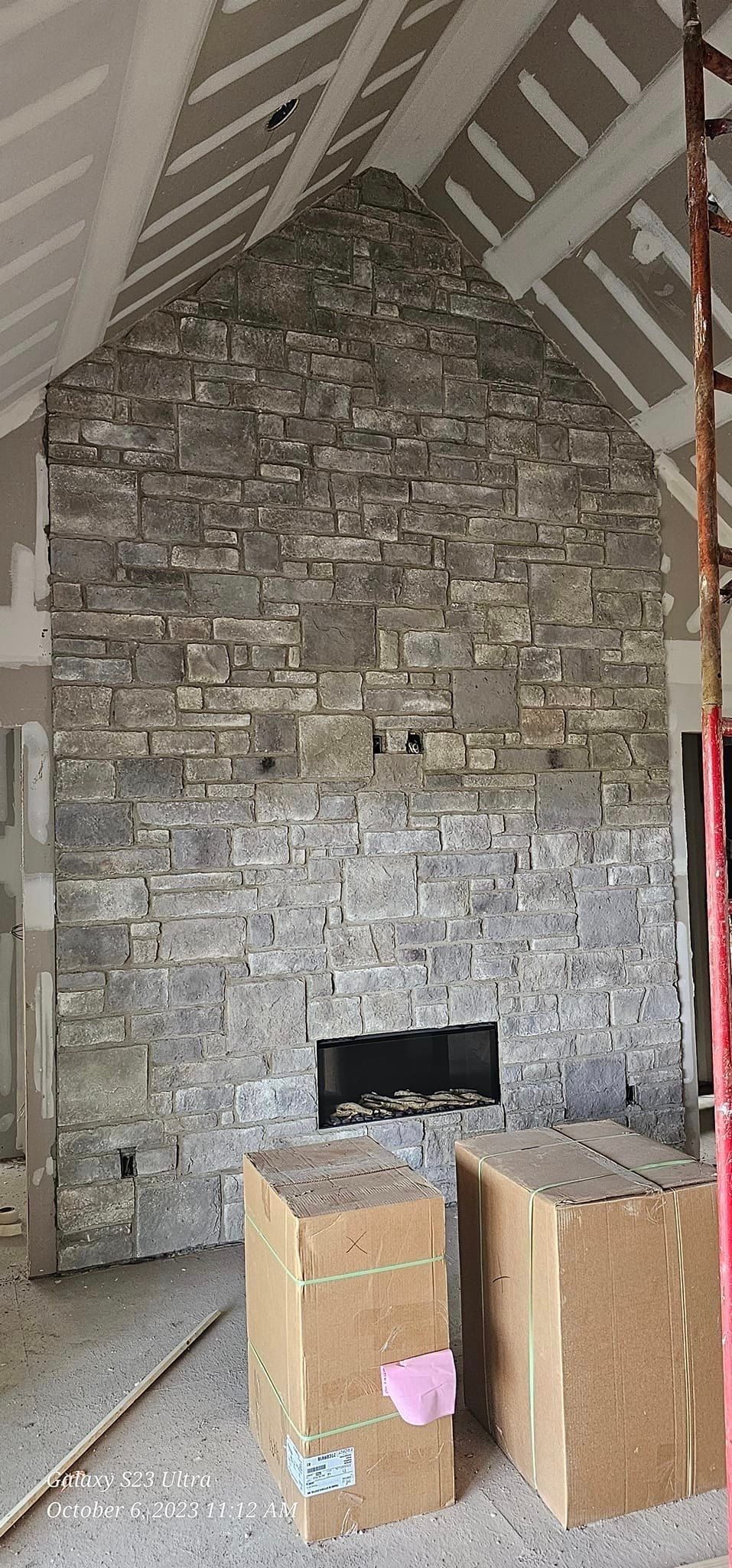 Stone fireplace in a room under construction, with cardboard boxes in front.