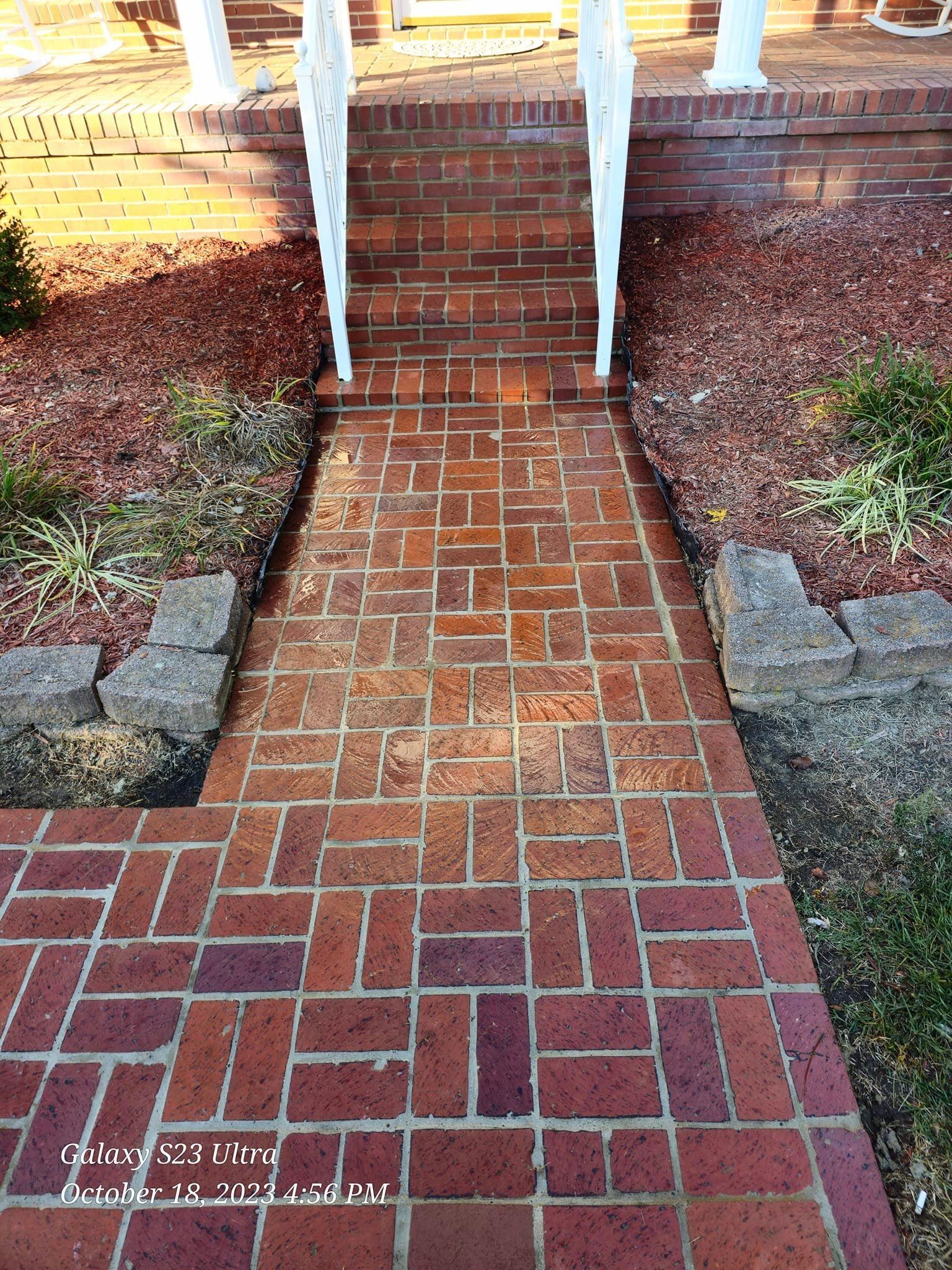 Brick walkway leading to brick steps and white railing. Red brick.