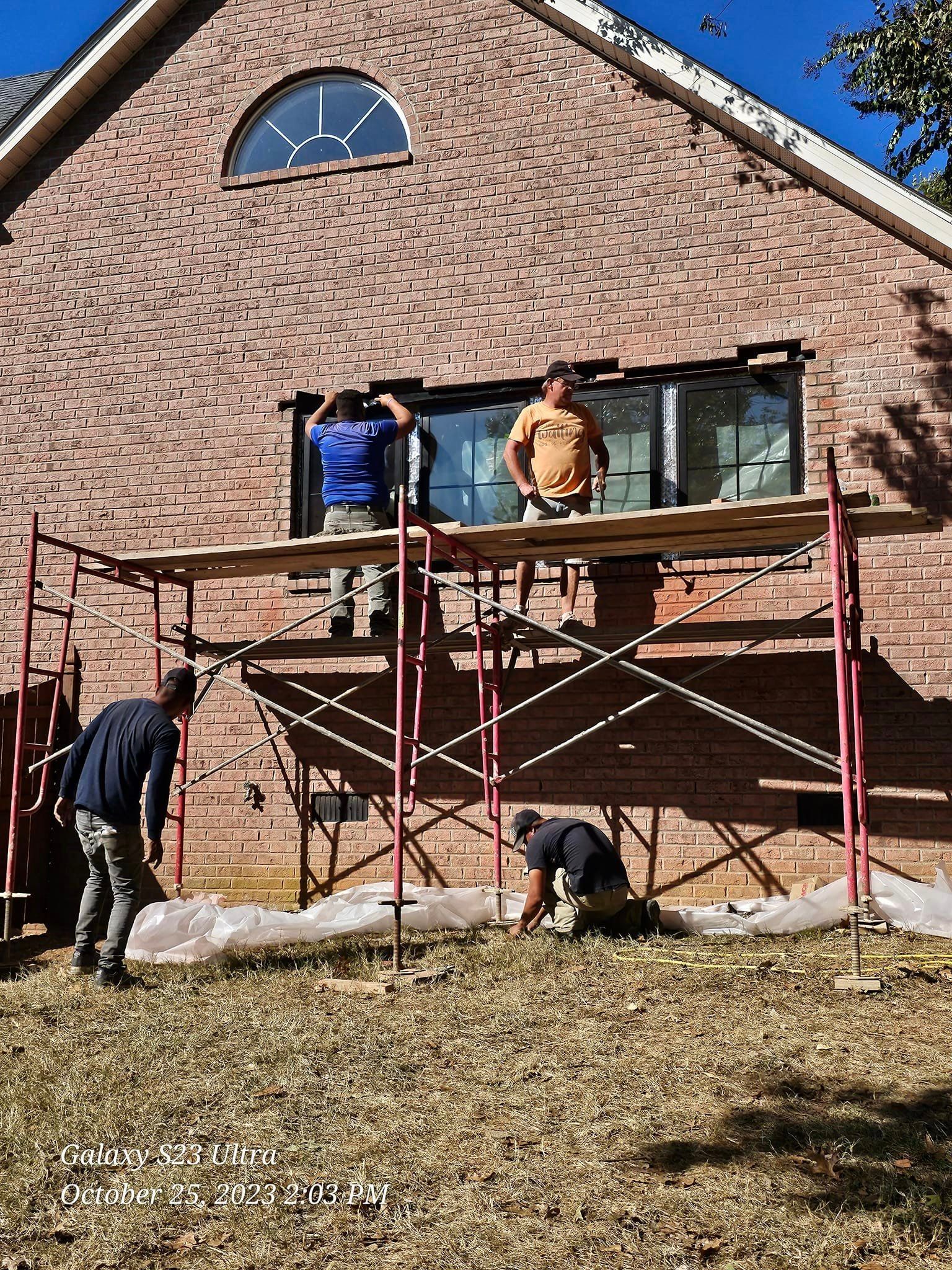 Workers installing a window on brick house, using a scaffolding.