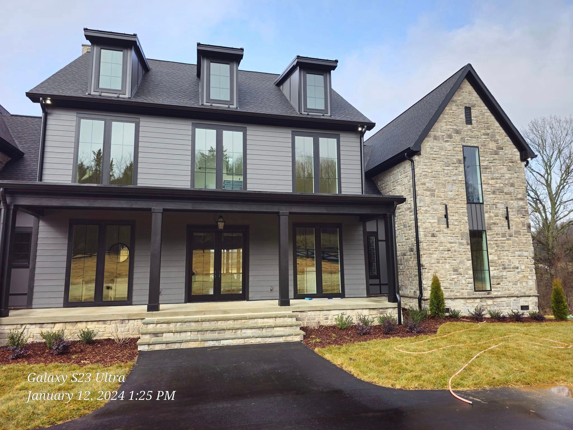 Gray house with black trim, stone addition, and a long driveway.
