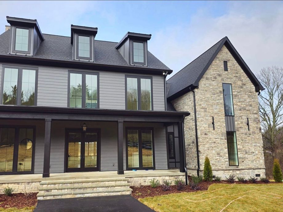 Two-story house with gray siding and stone facade, black trim, and tall windows, on a grassy lawn.