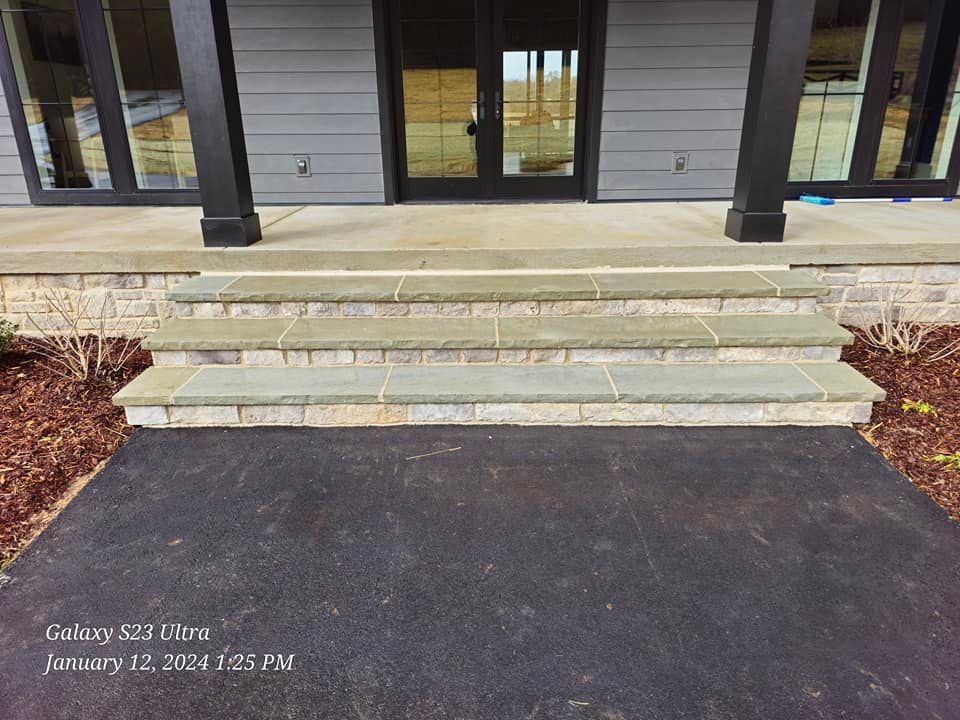 Stone steps leading up to a house with a black door and gray siding.