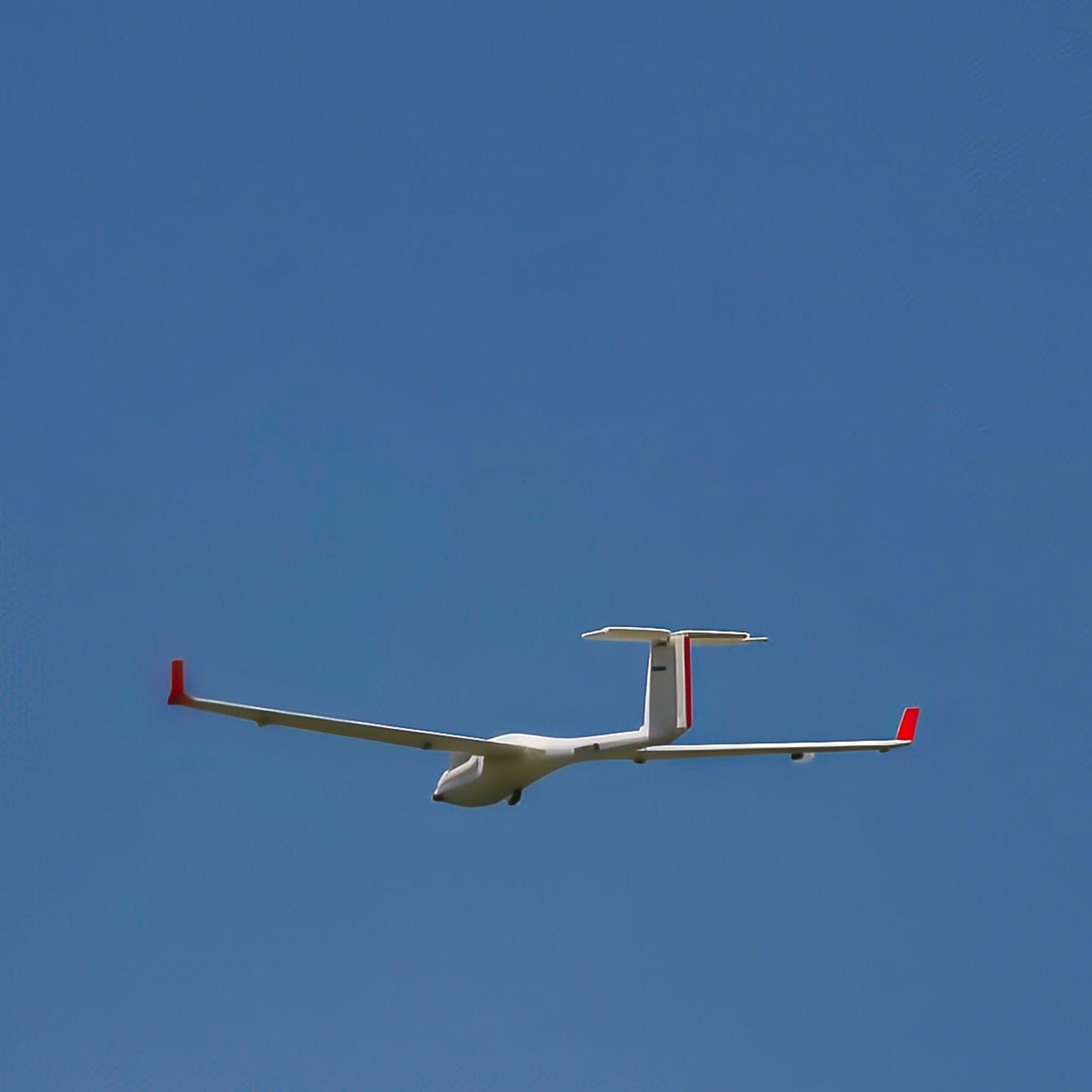 Glider soaring in a clear blue sky, white body, red wingtips and tail details.