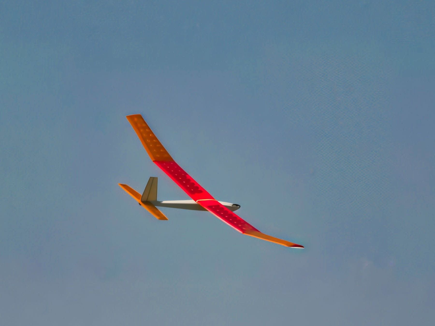 Glider with orange and red wings soaring against a clear blue sky.
