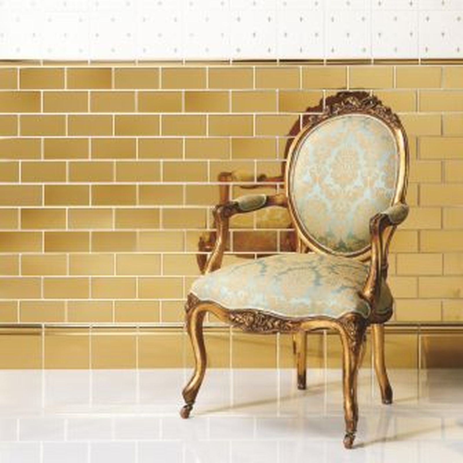 Ornate gold chair against a tiled wall of gold and white.