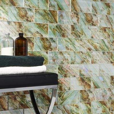 Bathroom wall with green and brown marble-look tiles, towels, and apothecary bottles on a black bench.