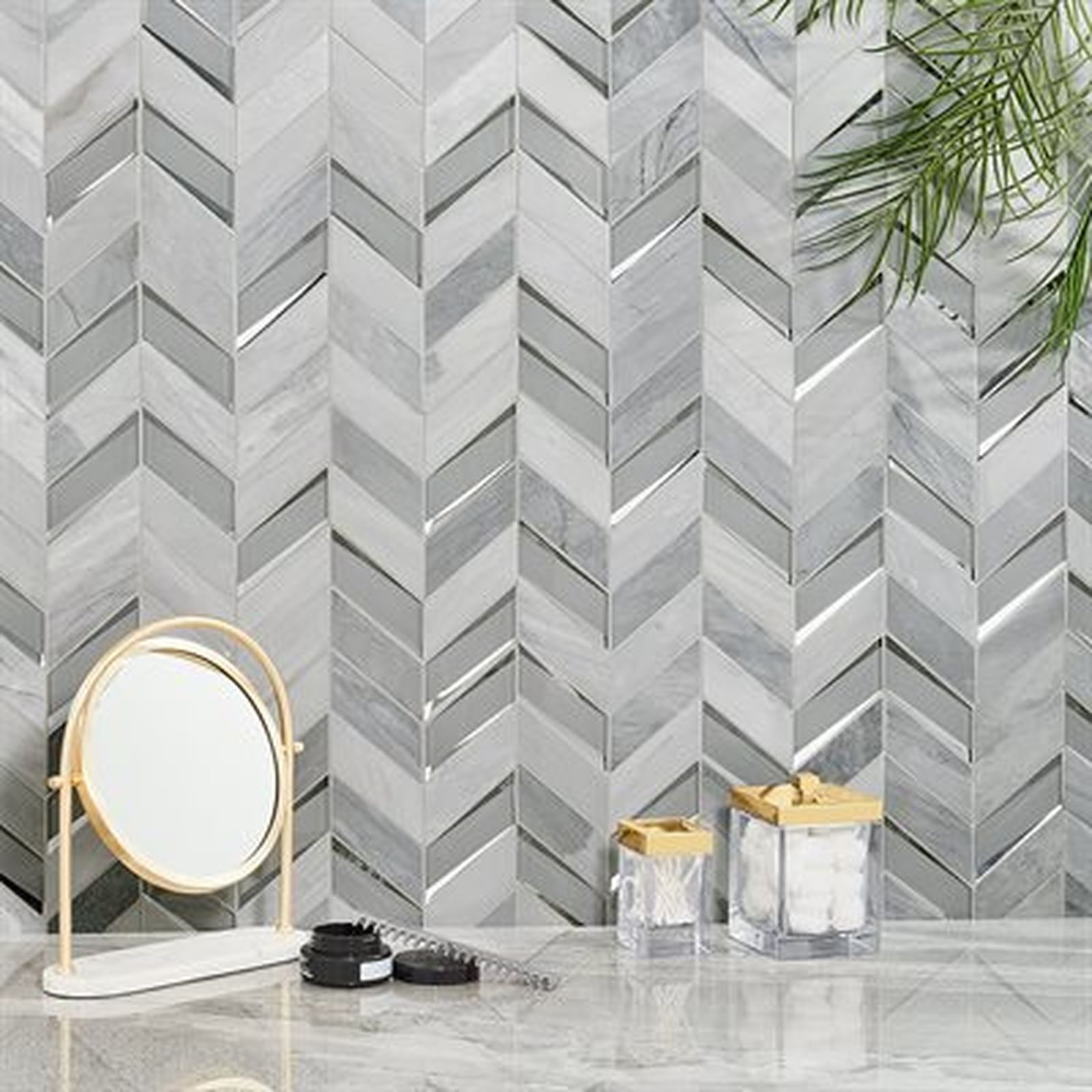 Herringbone tile wall in a bathroom, with a mirror and jars on a marble counter.