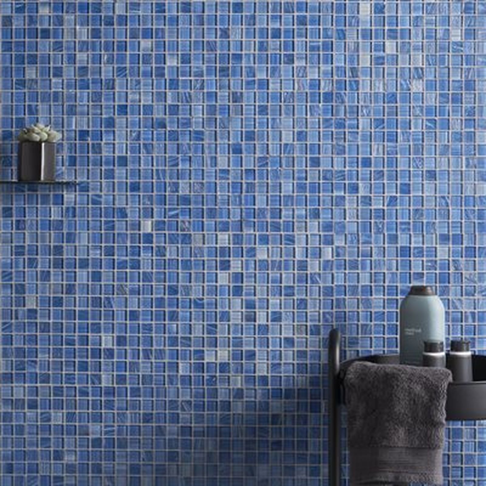 Blue mosaic tile bathroom wall with shelf, toiletries, and towel rack.