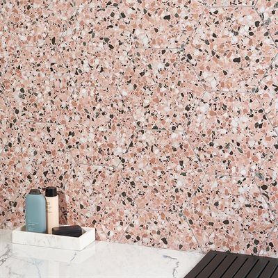 Pink terrazzo wall with bathroom essentials on a white shelf.