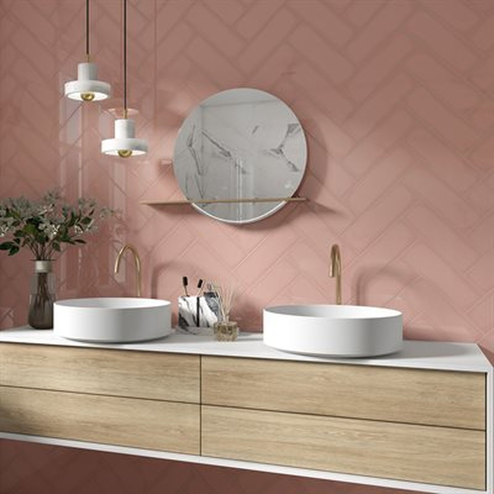 Pink herringbone tile bathroom with white sinks, wood vanity, and gold fixtures. Round marble mirror.