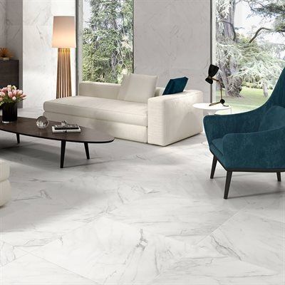 Living room with white marble floors, a white couch, and blue armchair, looking out onto trees.