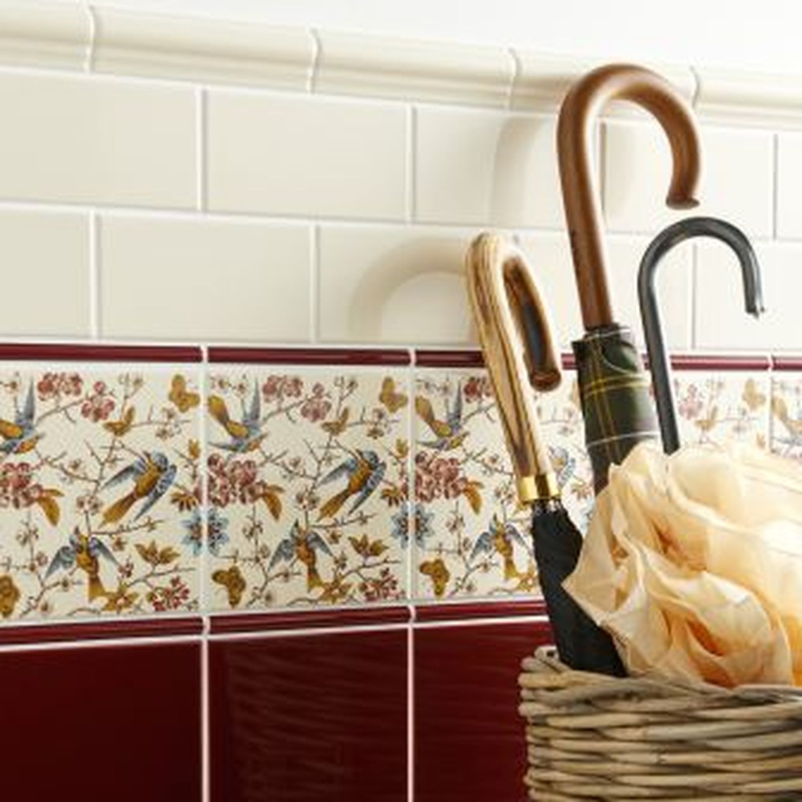 Decorative tiled wall with umbrellas in a basket. Floral border and maroon tiles.