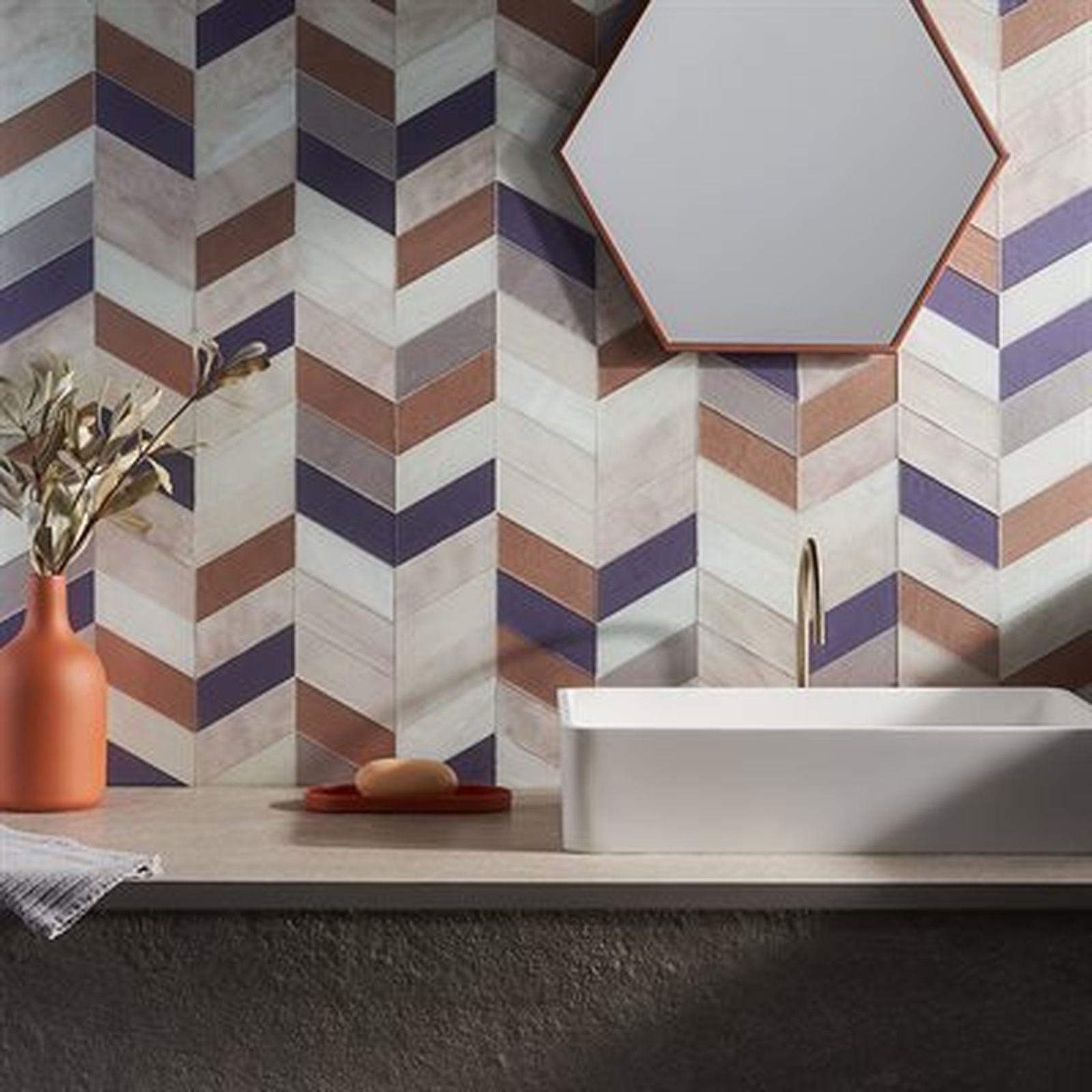 Bathroom with a chevron tile wall in shades of purple, brown, and white, a white sink, and a copper-framed mirror.
