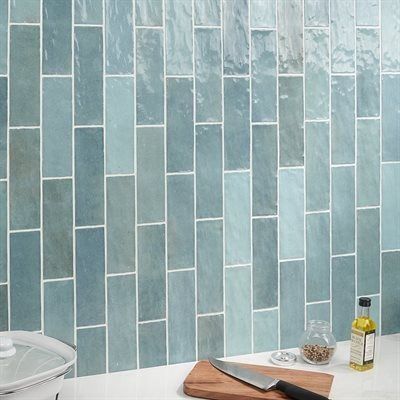 Blue-green rectangular tiles on a kitchen backsplash; white grout. A cutting board with a knife and seasonings.