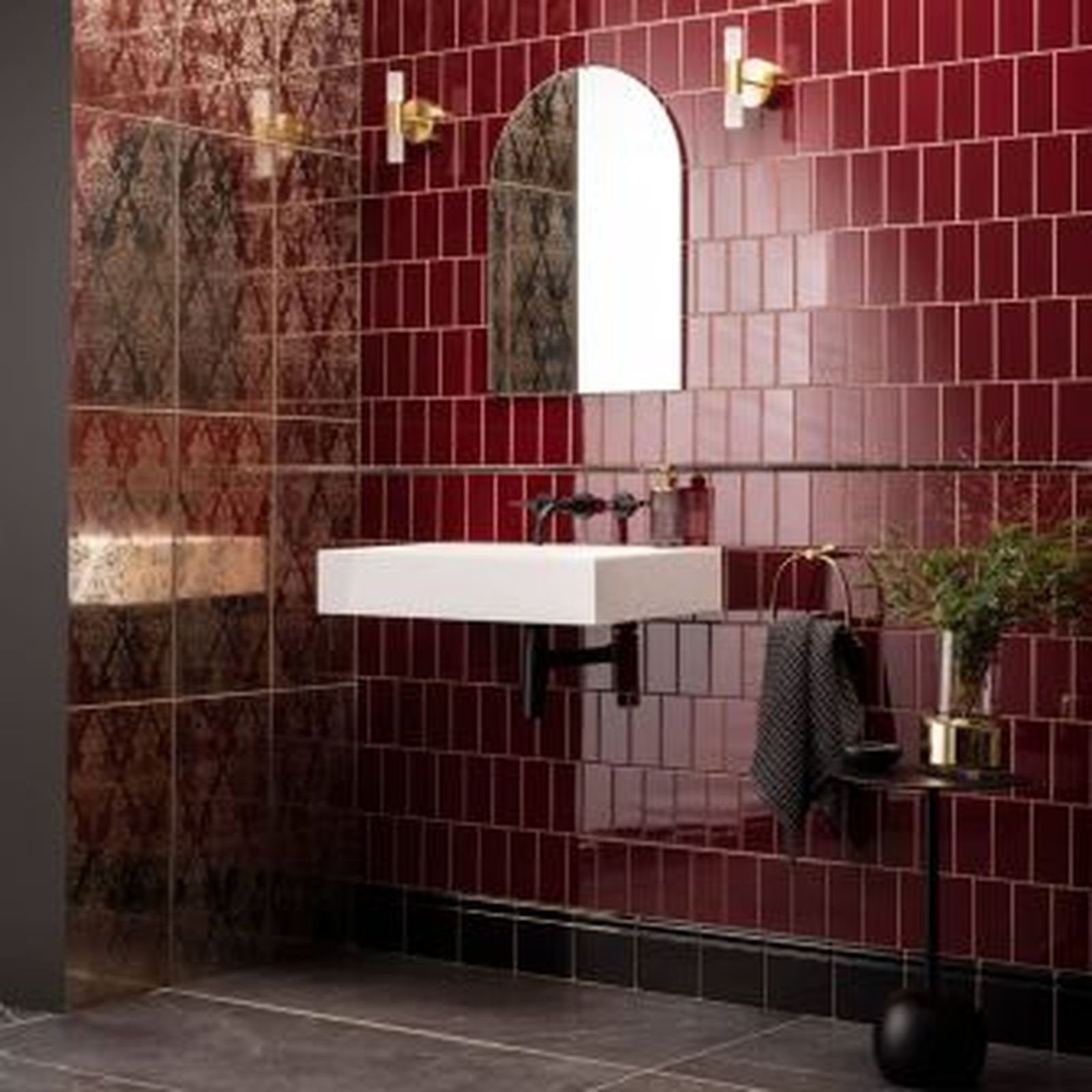 Red-tiled bathroom with a white sink, gold accents, a black towel, and a small side table.