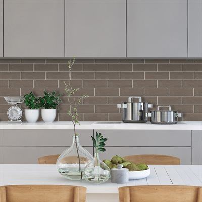 Kitchen with gray cabinets, brick-style backsplash, stainless steel pots, and a white table with plants.
