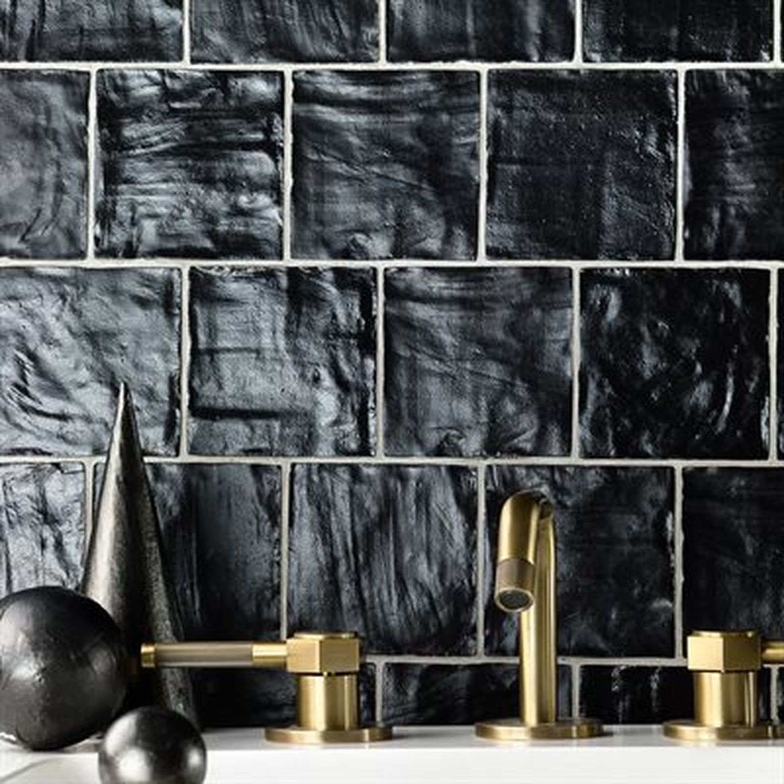 Close-up of black textured tiles and gold bathroom fixtures.
