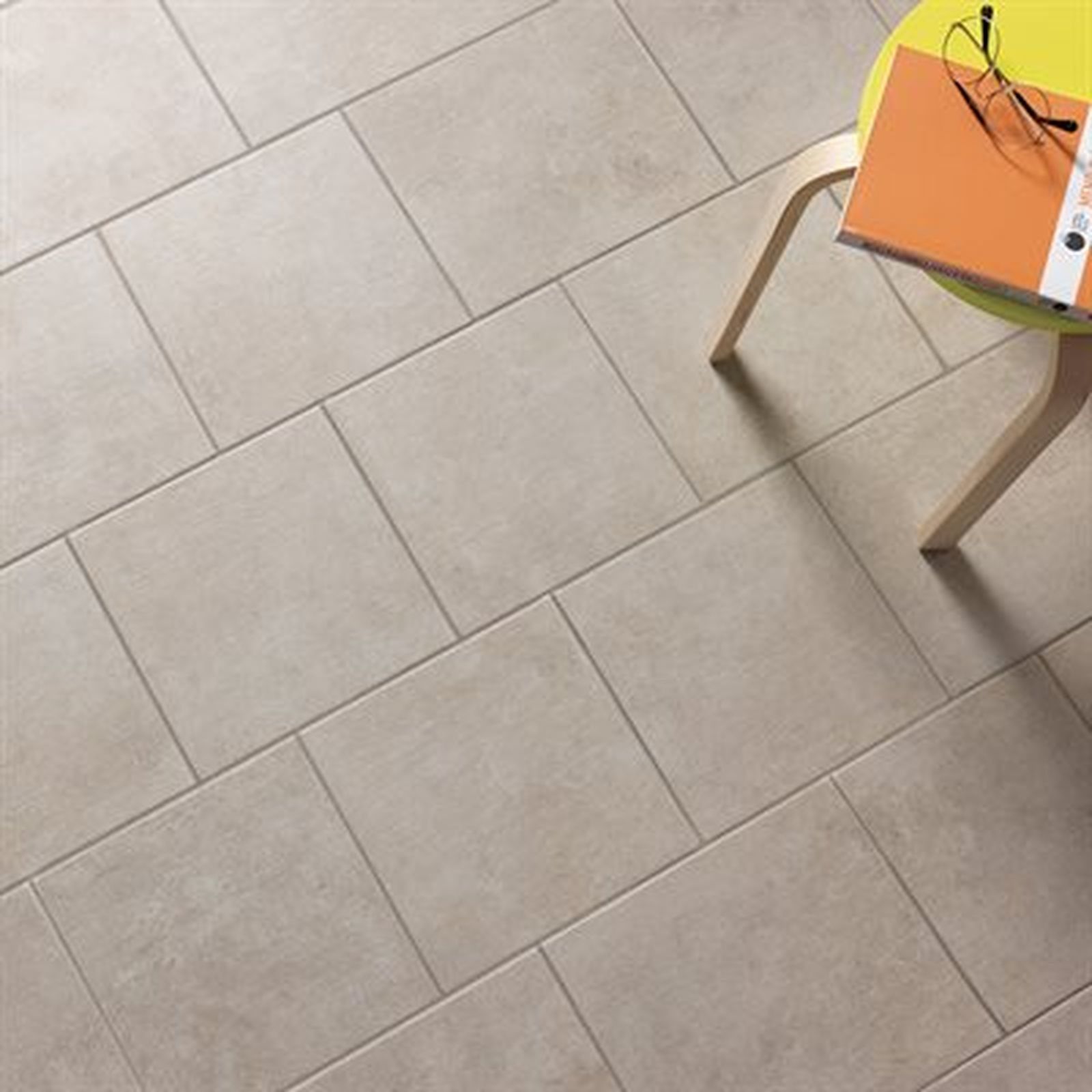 Beige tiled floor with a yellow chair holding a book and glasses.