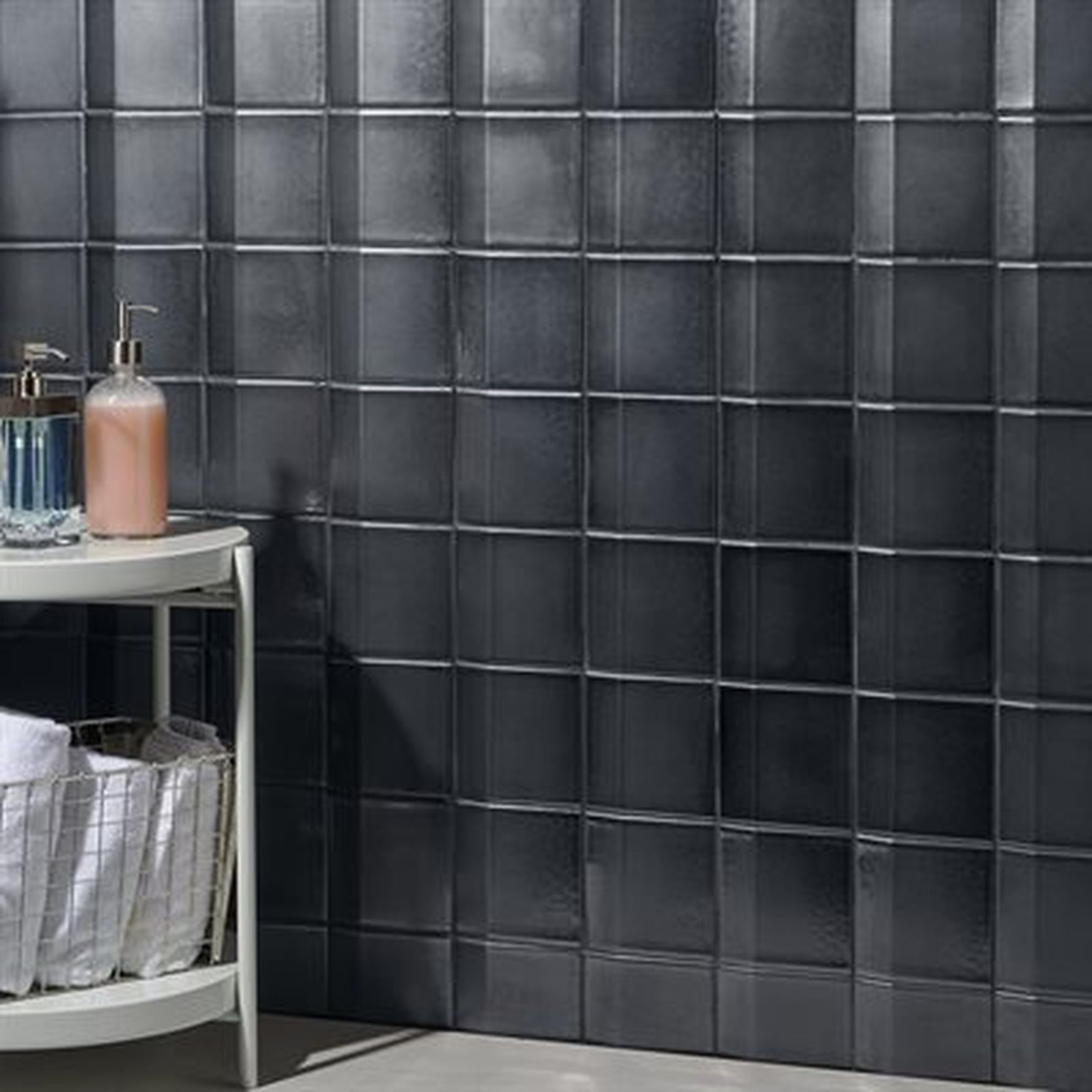 Dark gray tiled bathroom wall with a small side table and toiletries.