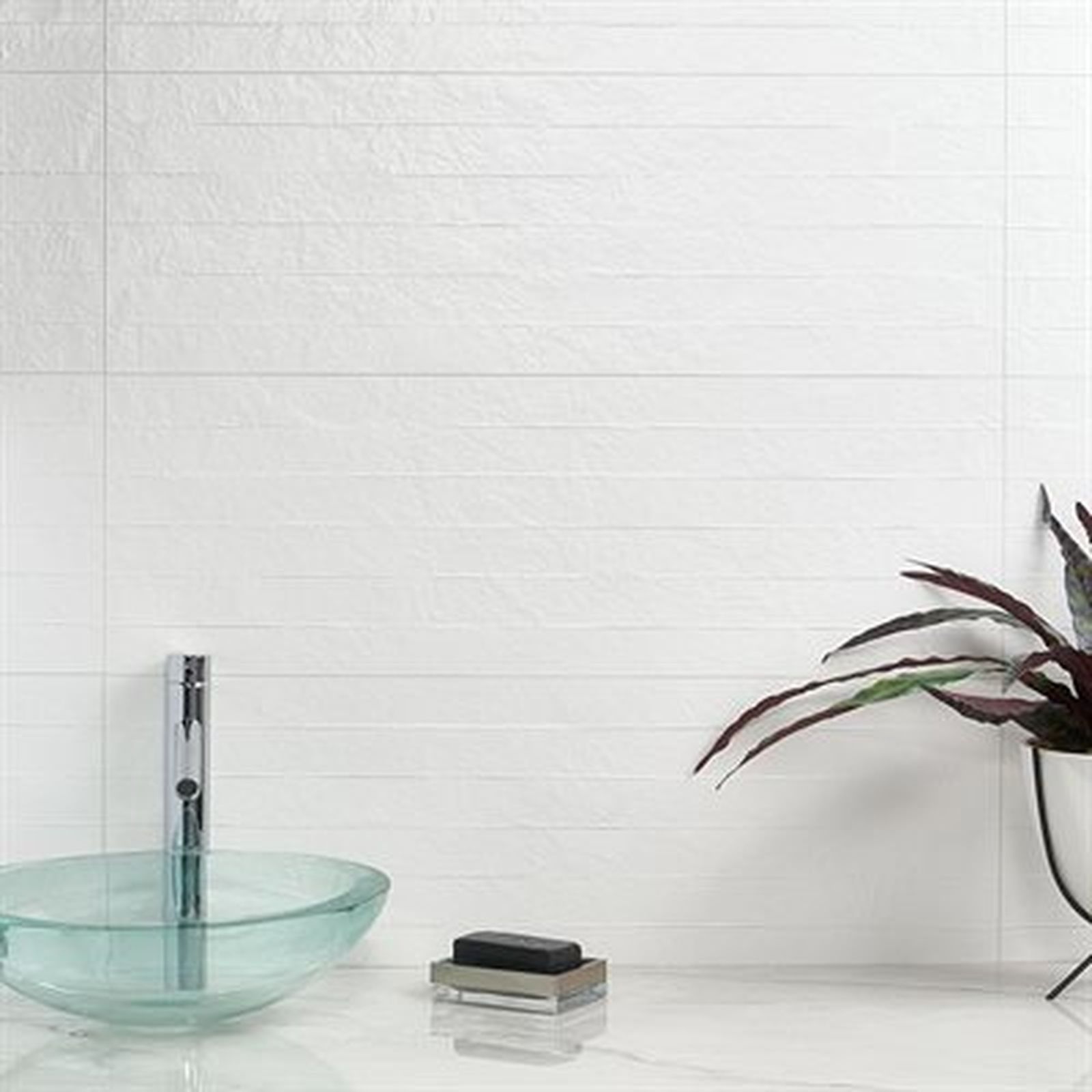 Bathroom with white textured tile wall, glass sink, soap, and plant.