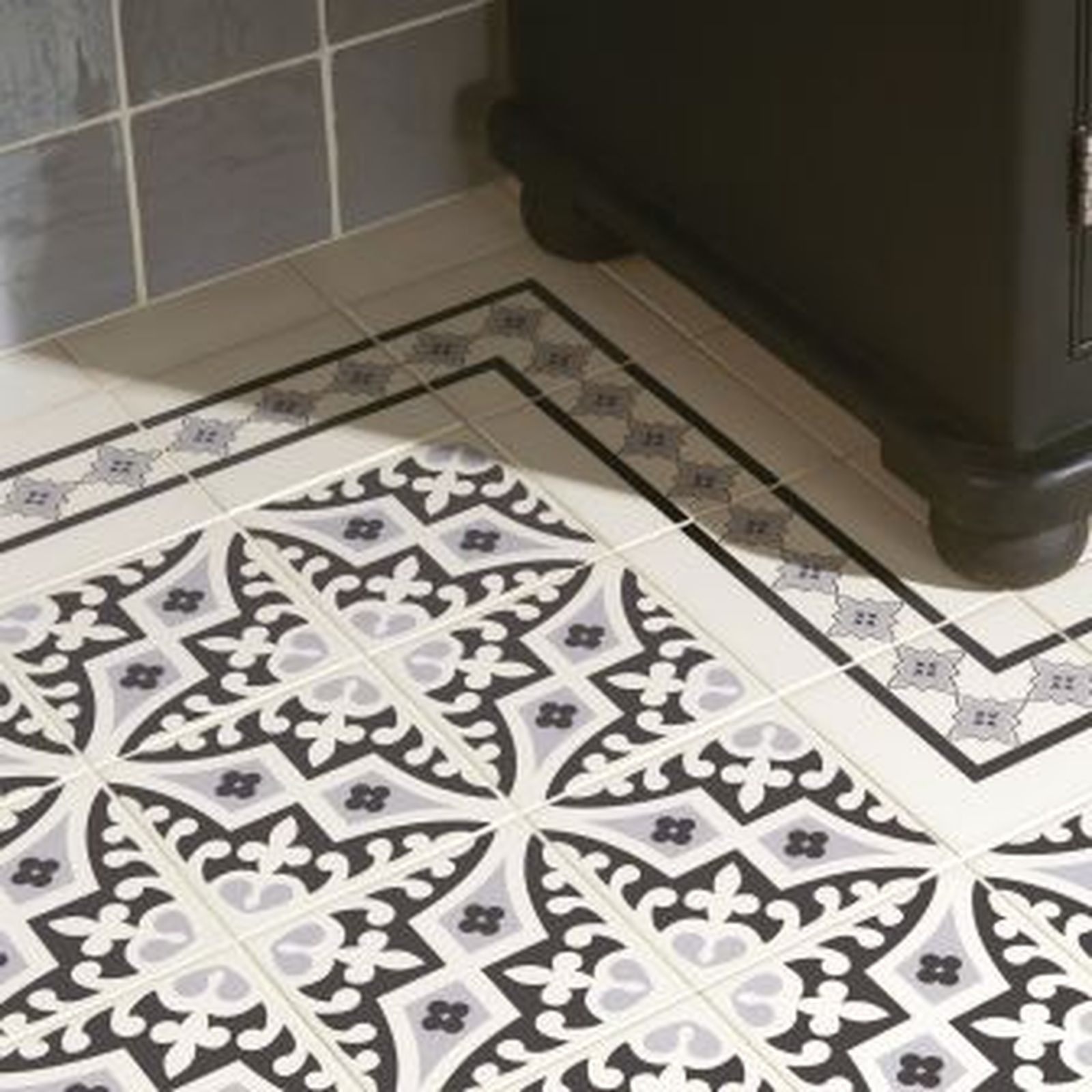 Patterned bathroom floor tiles with a decorative border, black cabinet.