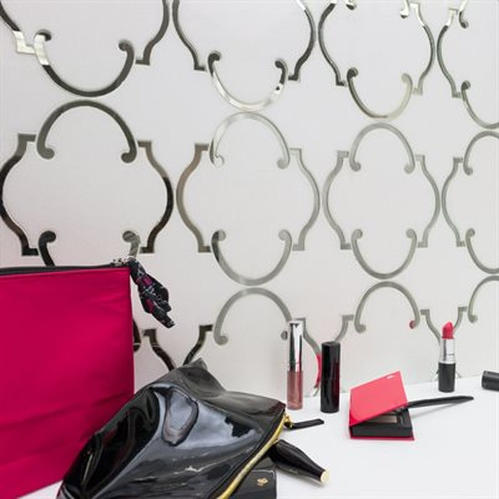 Makeup products next to a patterned white wall. A bright pink bag and a black bag are on the table.