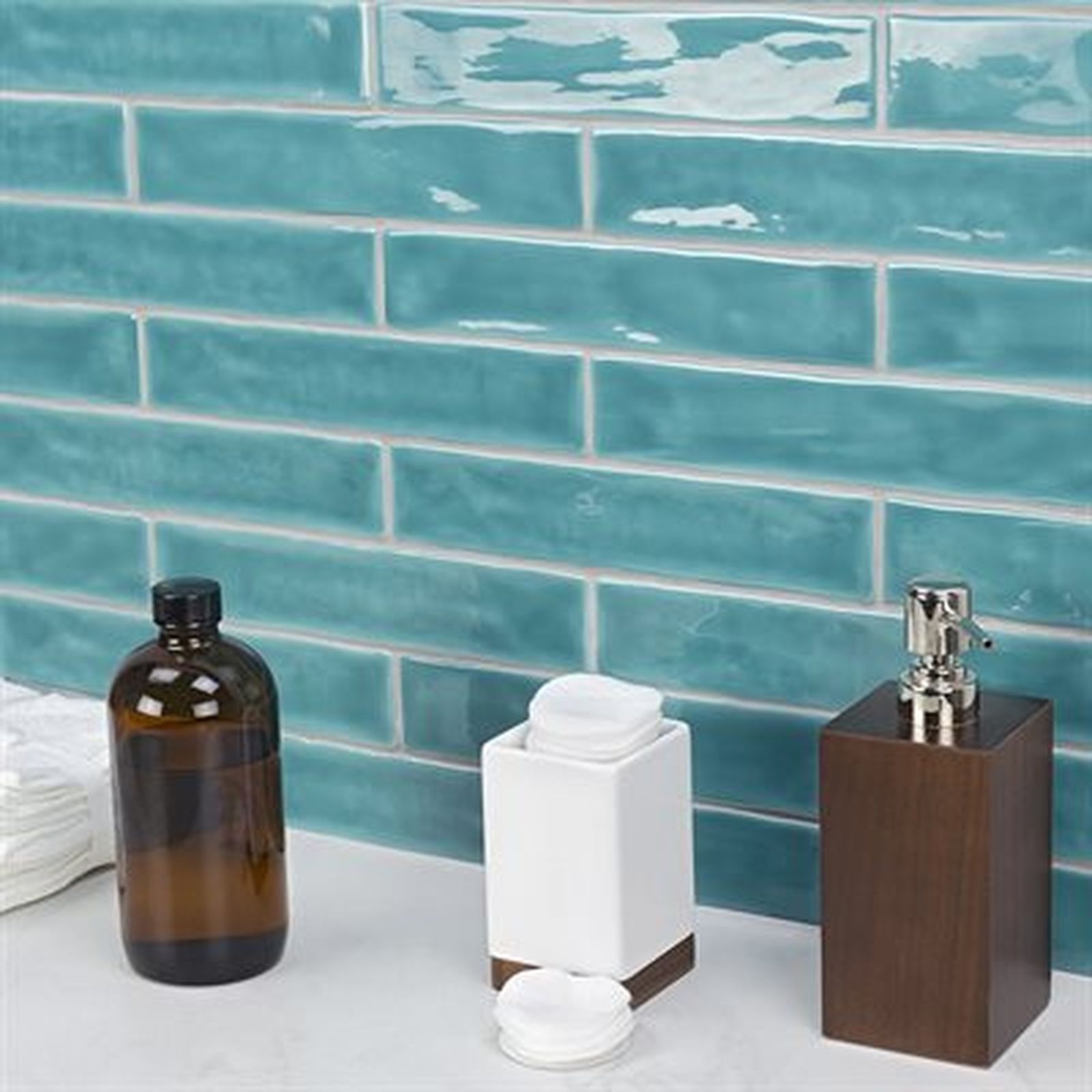 Teal subway tile backsplash with white grout, a vanity with toiletries: amber bottle, dispenser, and cotton pads.