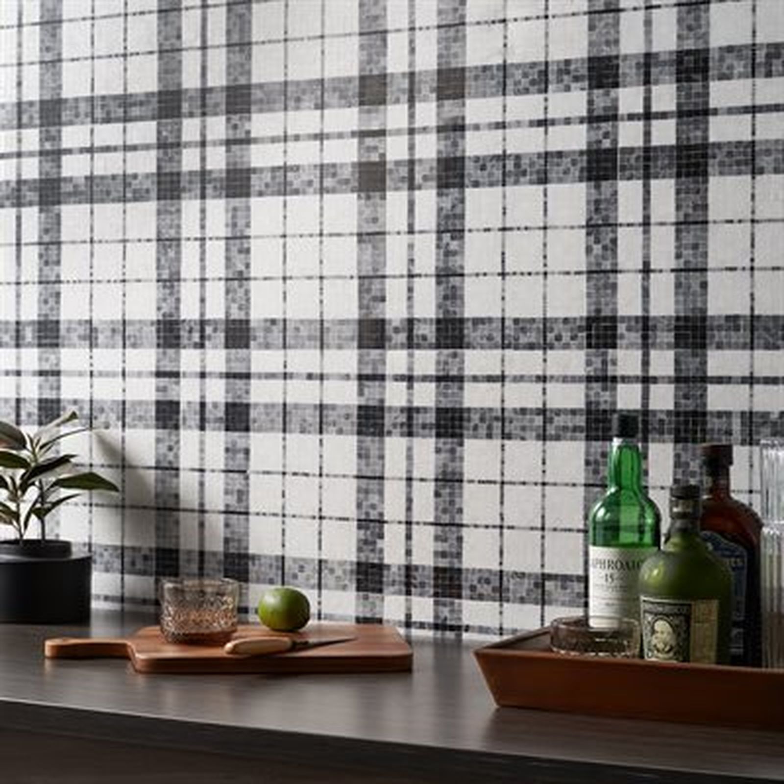 Black and white plaid wallpaper behind a countertop with liquor bottles, a cutting board, and a plant.