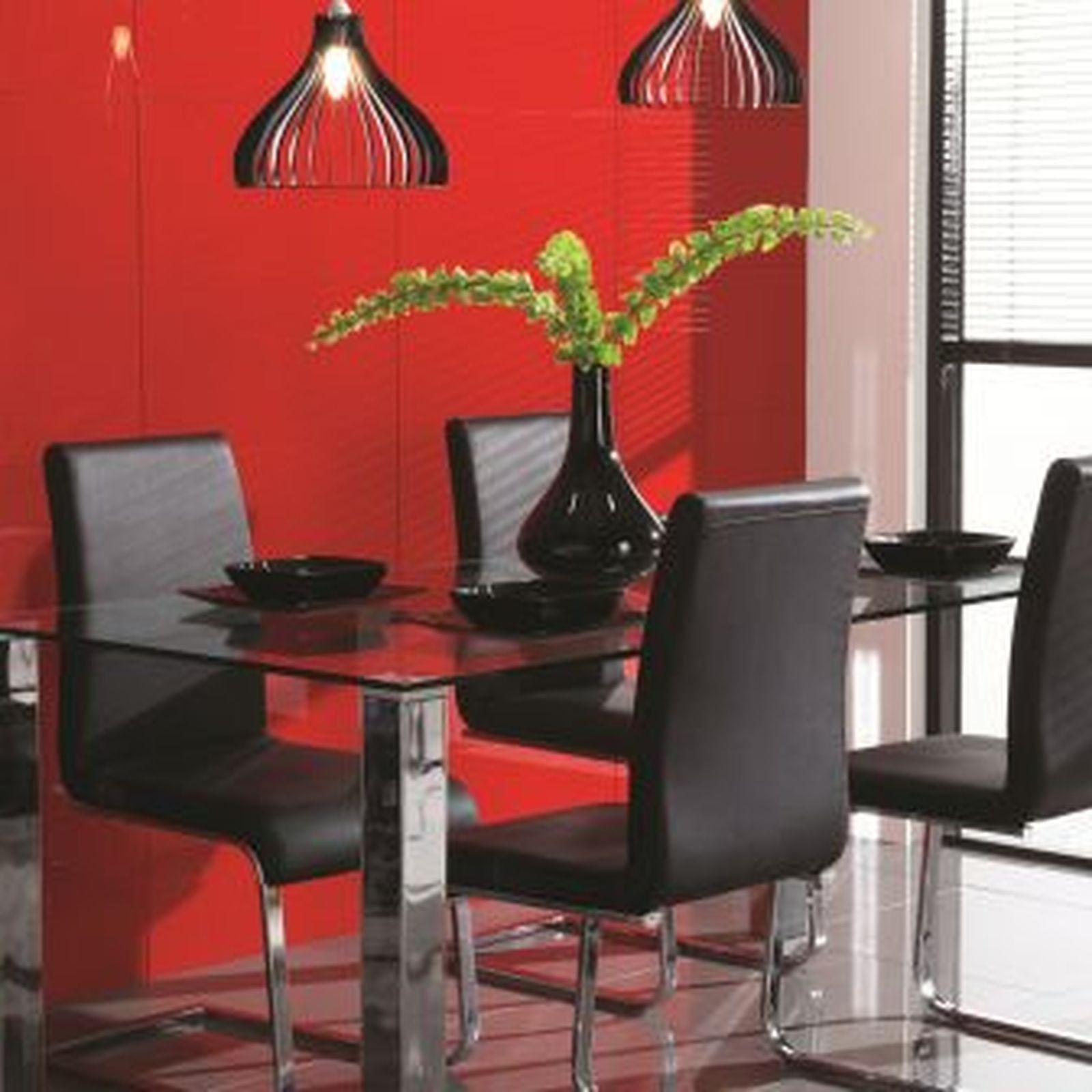 Modern dining room with glass table, black chairs, red wall, black pendant lights, and vase of green flowers.
