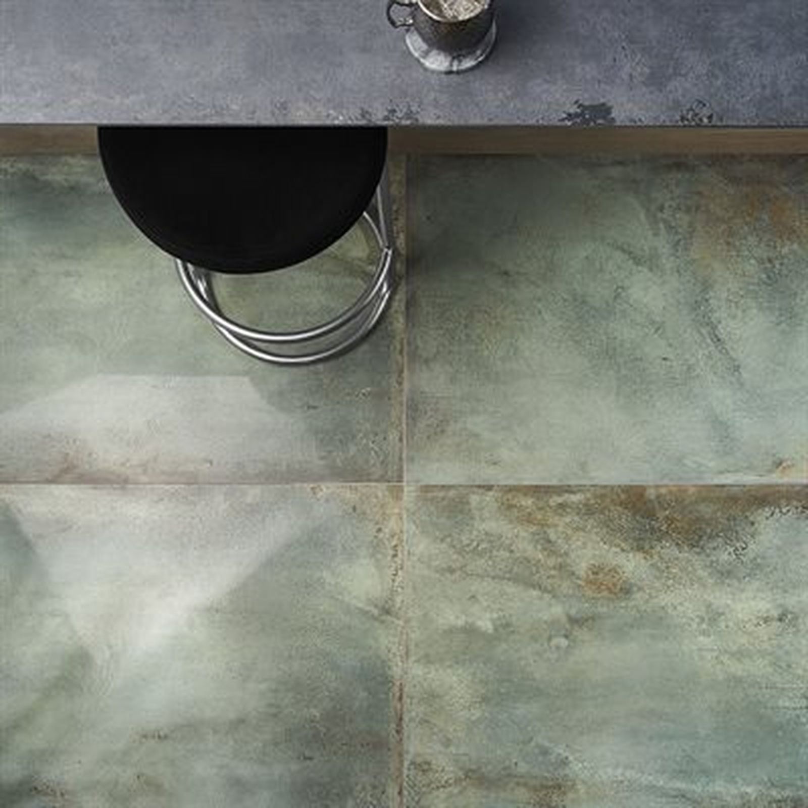 Overhead view of a teal-toned tile floor with a black stool and a cup on a counter.