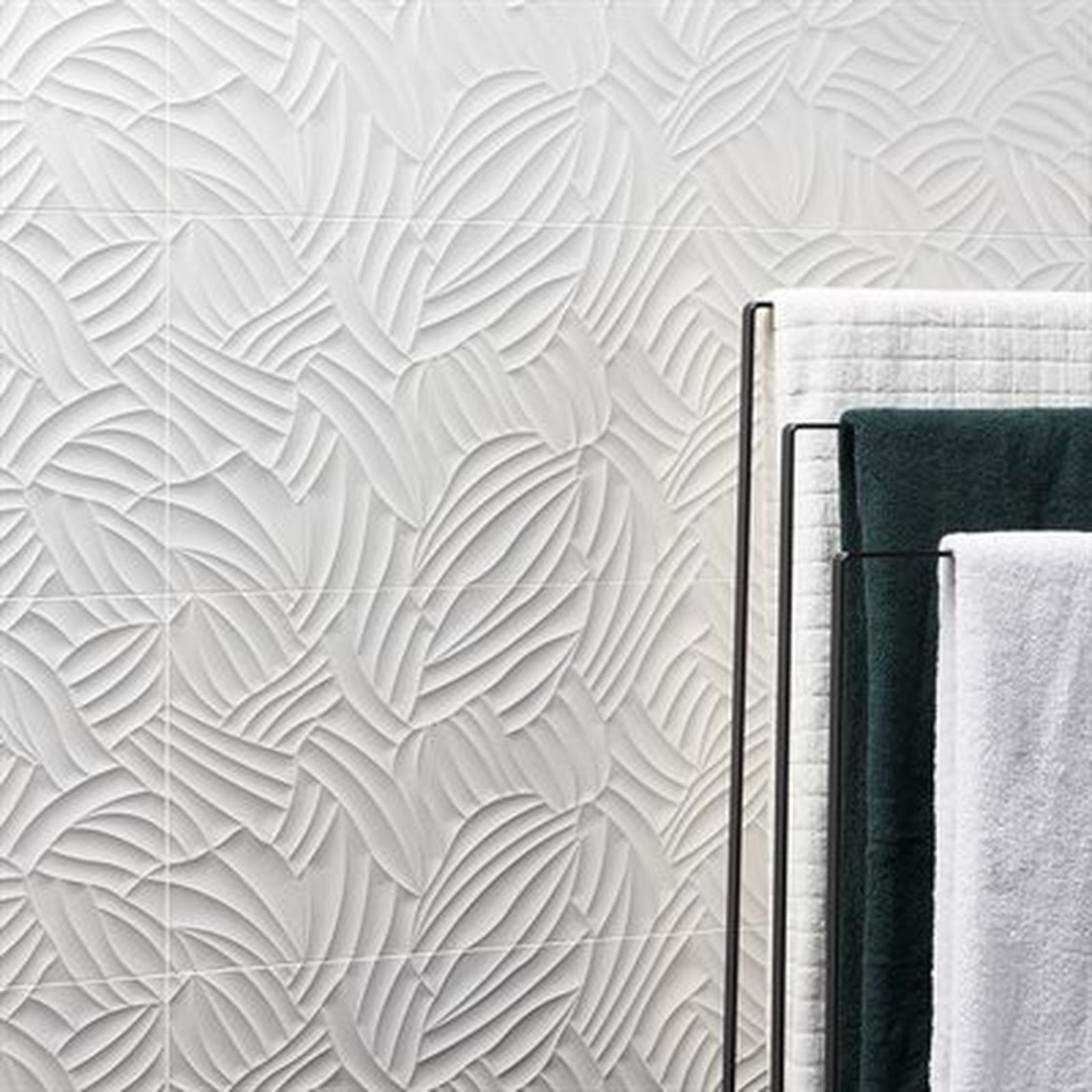 Textured white tile wall with stylized leaf pattern. Towel rack holds green and white towels.