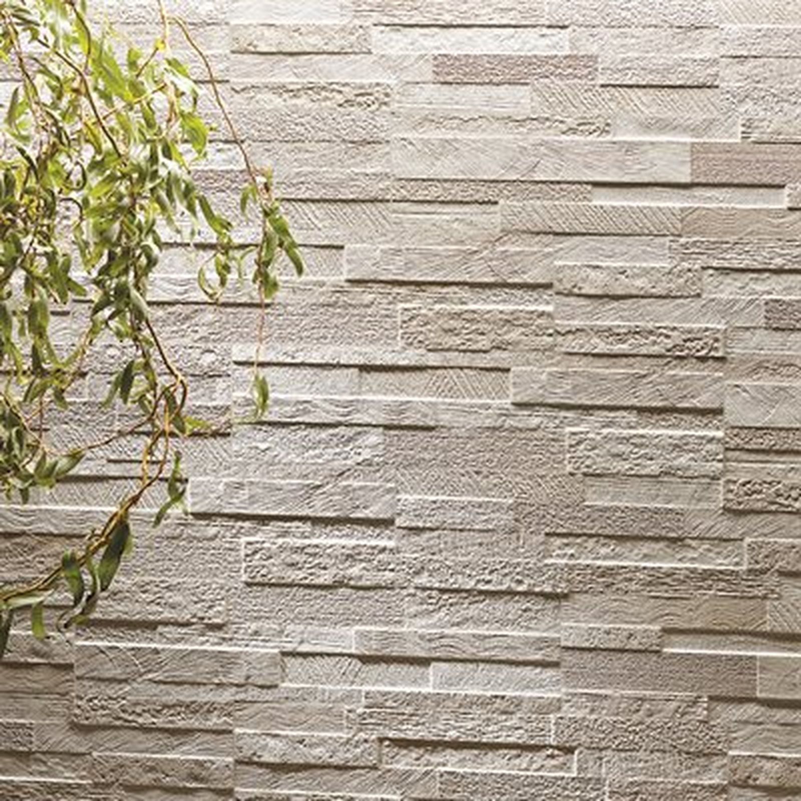 Textured stone wall with greenery in the corner.