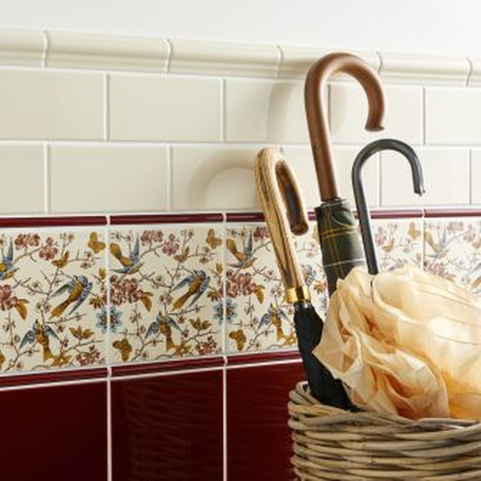 Two umbrellas in a wicker basket against a tiled wall with decorative floral and red accents.