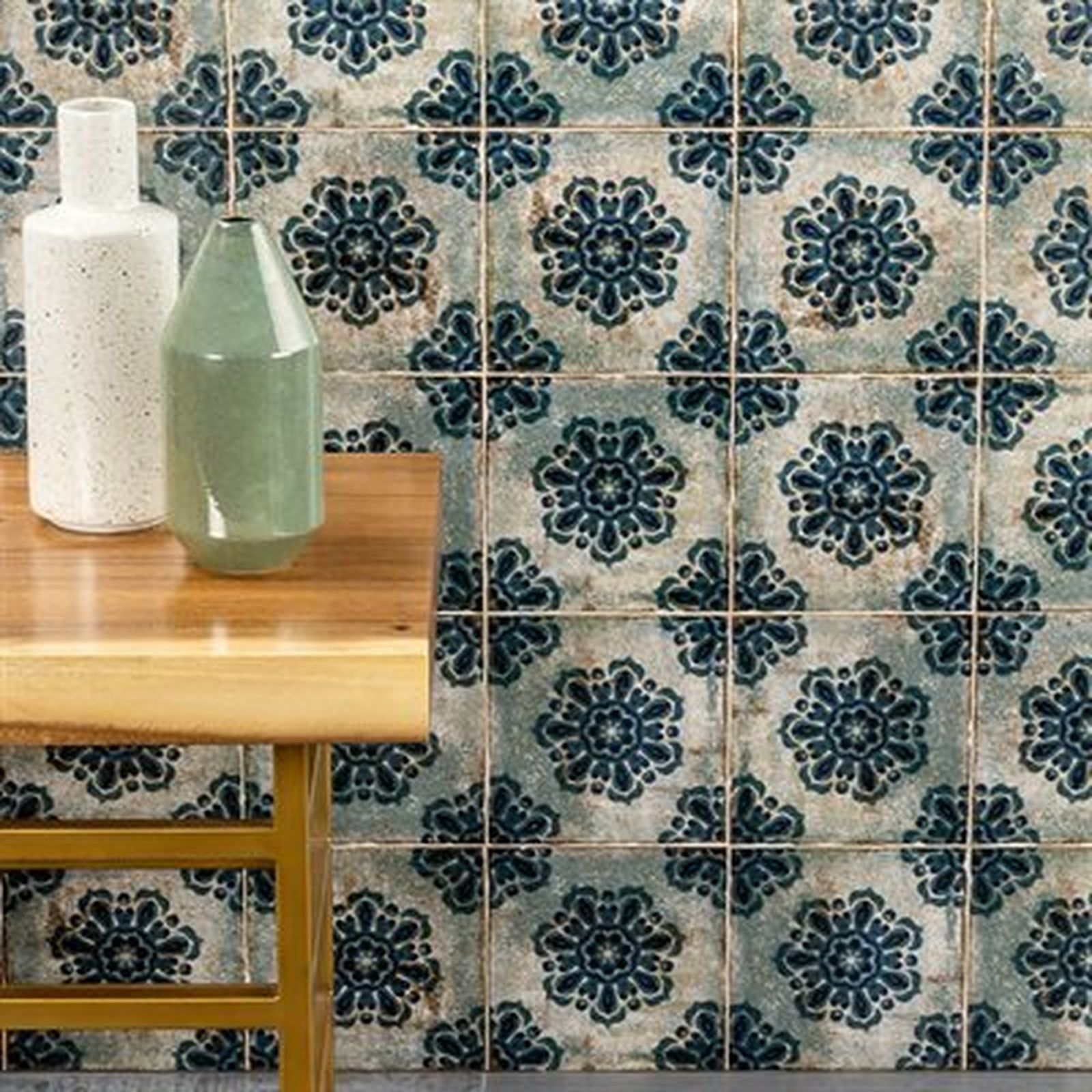 Two vases on a wooden table, against a wall of blue patterned tiles.