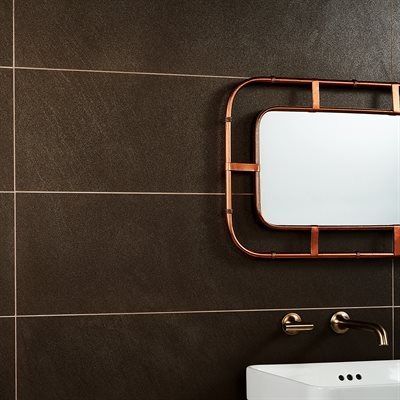 Dark brown tiled bathroom wall with copper-framed mirror, faucet, and sink.