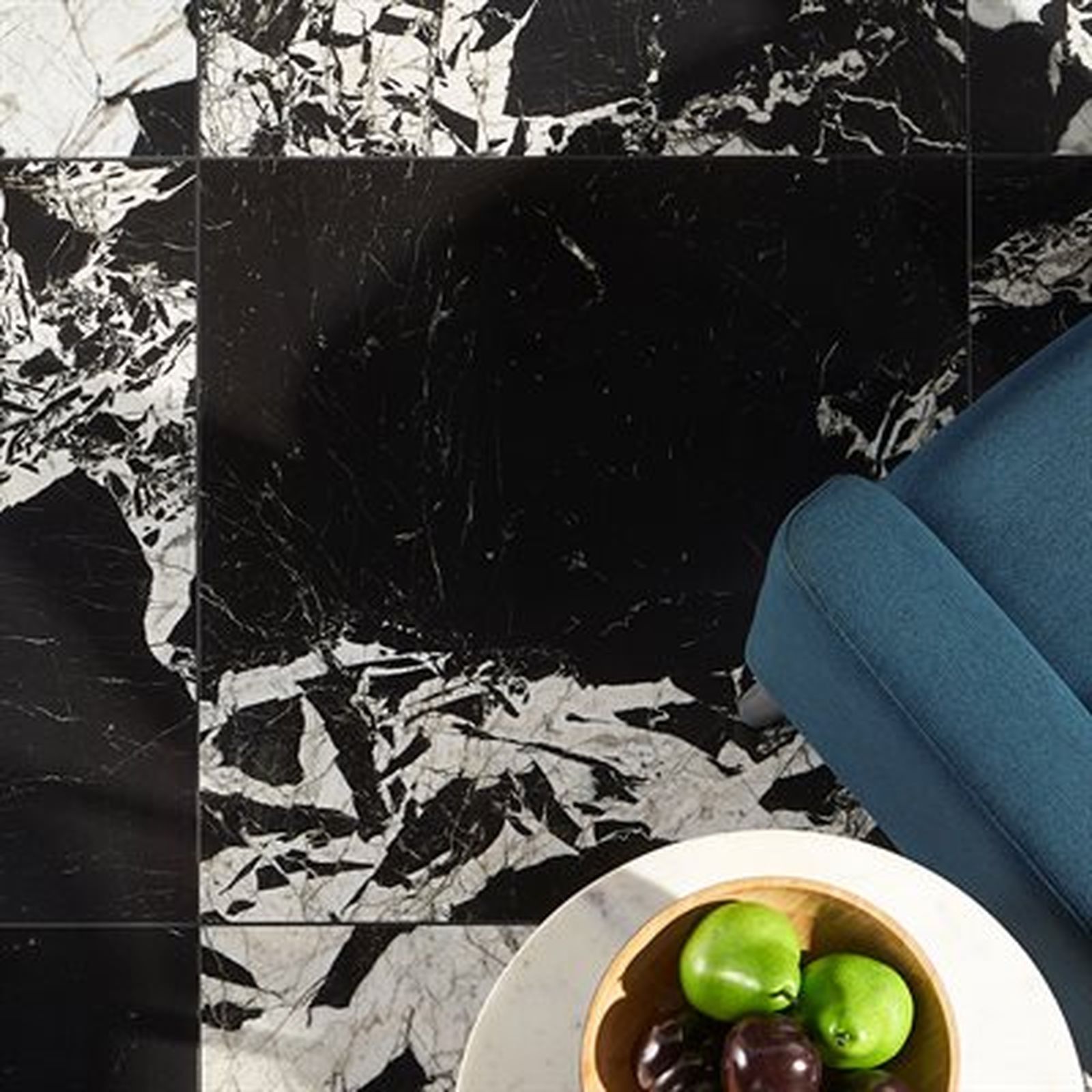 Black and white marble tile floor with a blue armchair and fruit bowl on a small table.