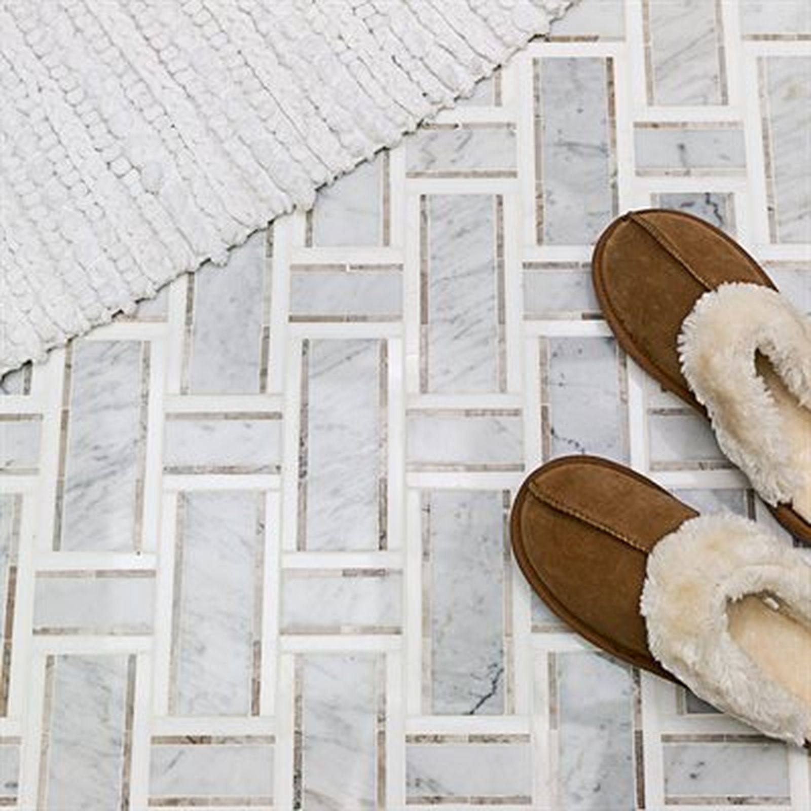 Brown slippers on marble bathroom floor, with white bath mat in the corner.