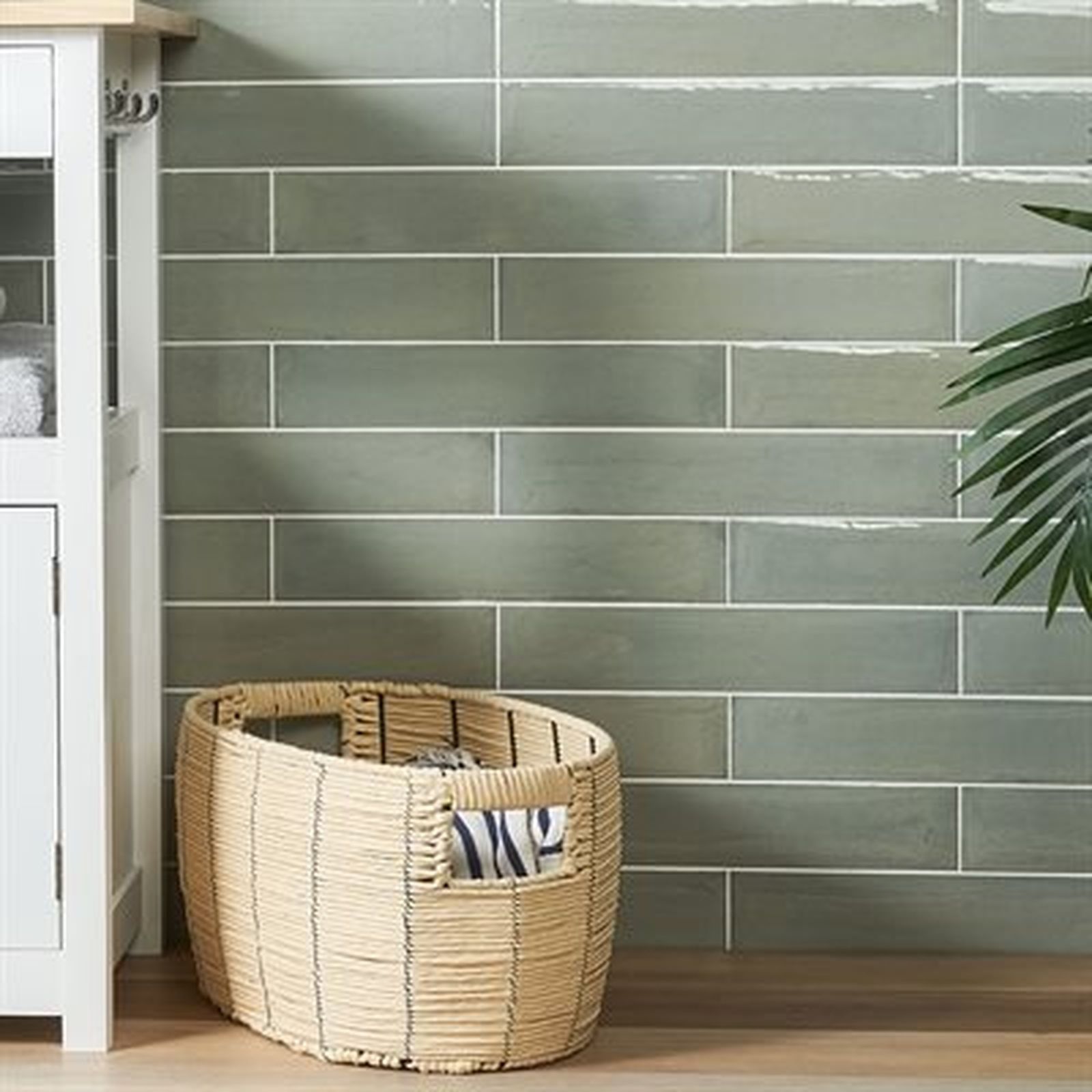 Bathroom with olive green rectangular tiles, a woven basket, and a plant.