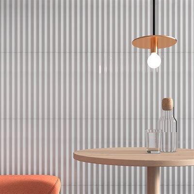 Gray ribbed wall with a round wooden table, water bottle, lamp, and orange chair.