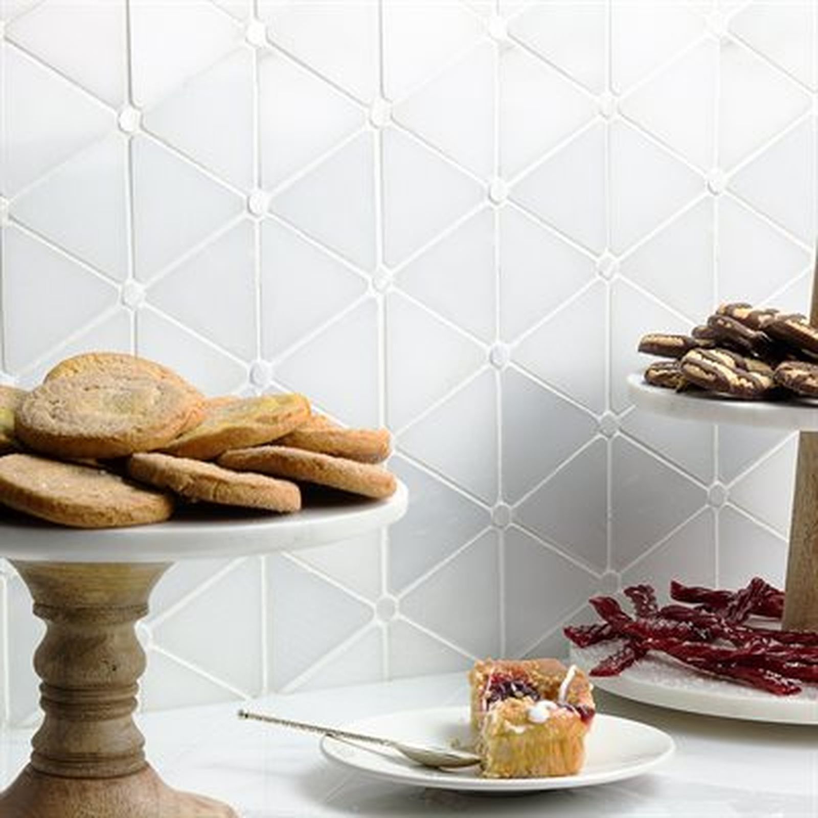 Cookies and pastries on marble serving dishes in front of a white geometric tile backsplash.
