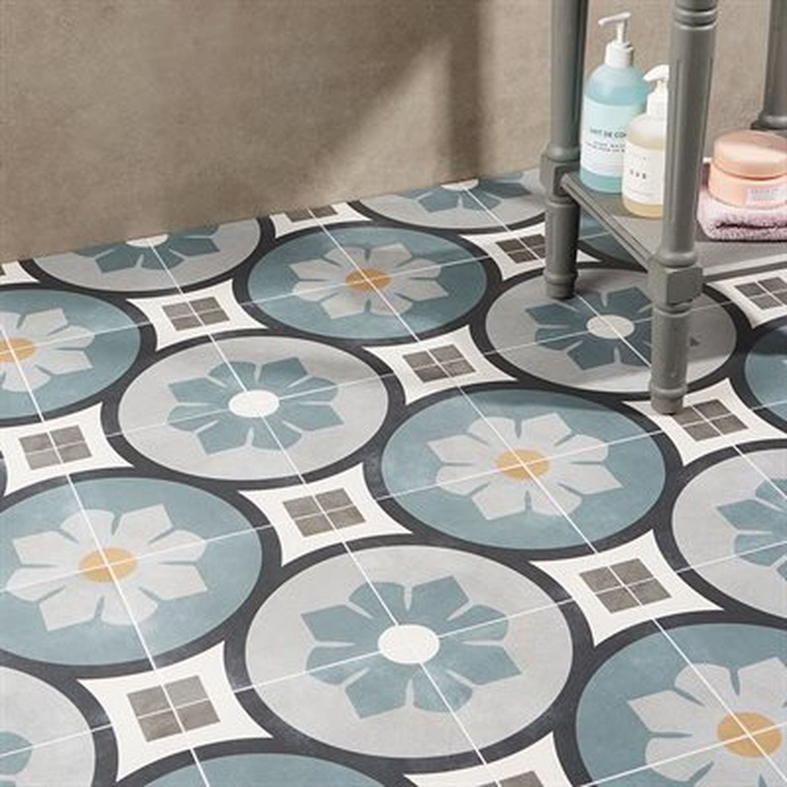 Floor tiles with a floral pattern in gray, blue, and white; a small shelf unit with toiletries stands on the tiles.