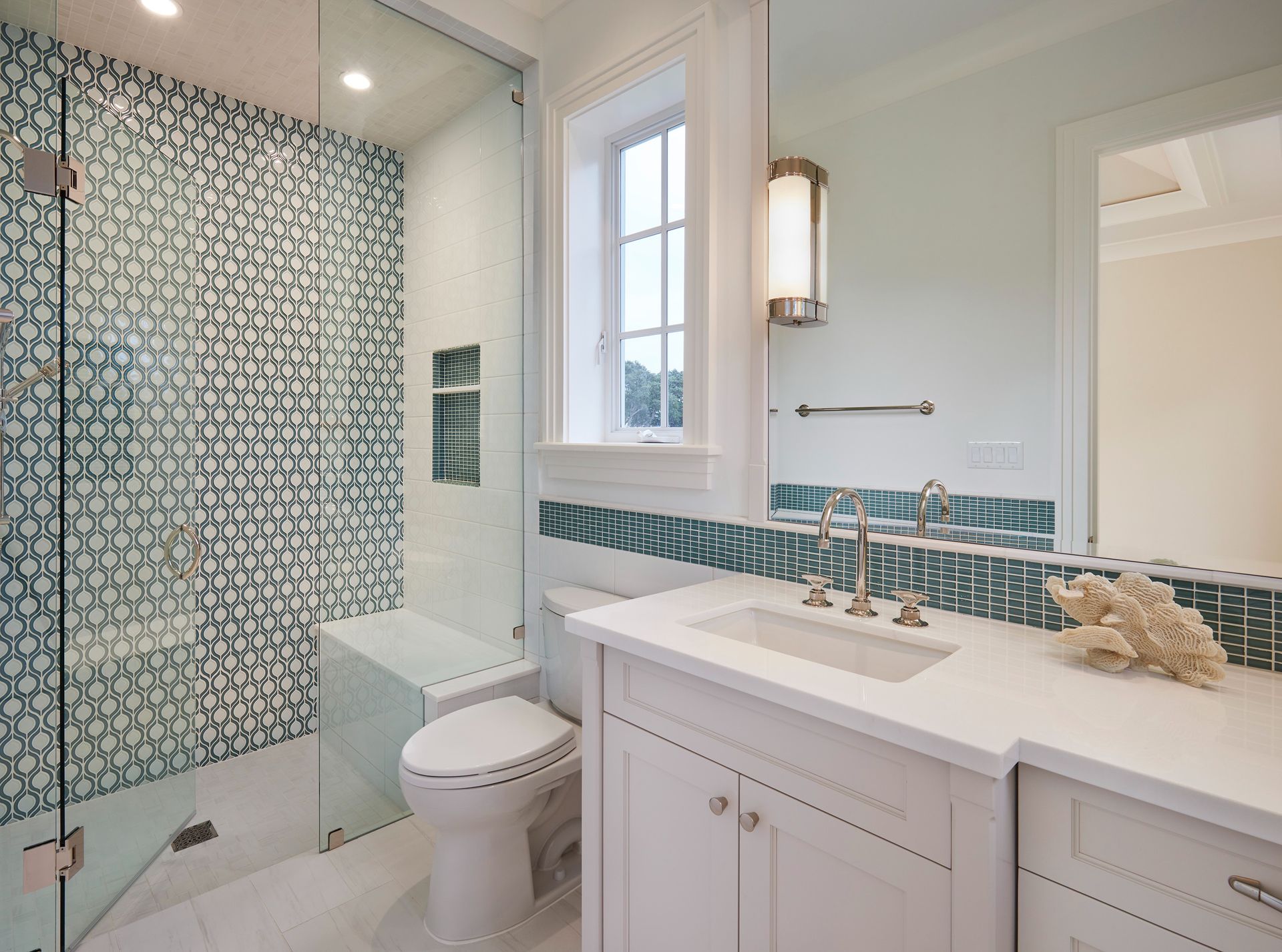 Bathroom with glass shower, blue mosaic tiles, white vanity, and window.