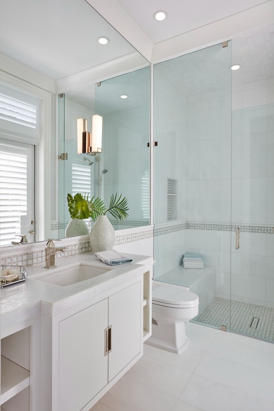 White bathroom with glass shower, white vanity, and toilet.