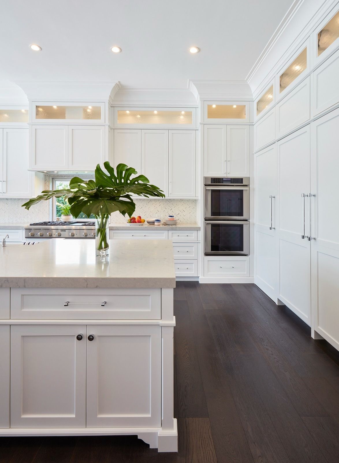 White kitchen with dark wood floors, island, and built-in appliances.