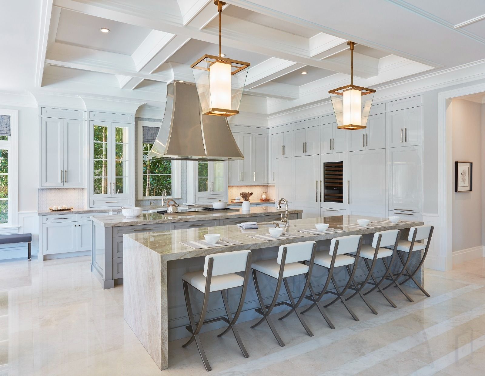 Spacious, light-filled white kitchen with two islands, marble countertops, stainless range hood, and gold pendant lights.